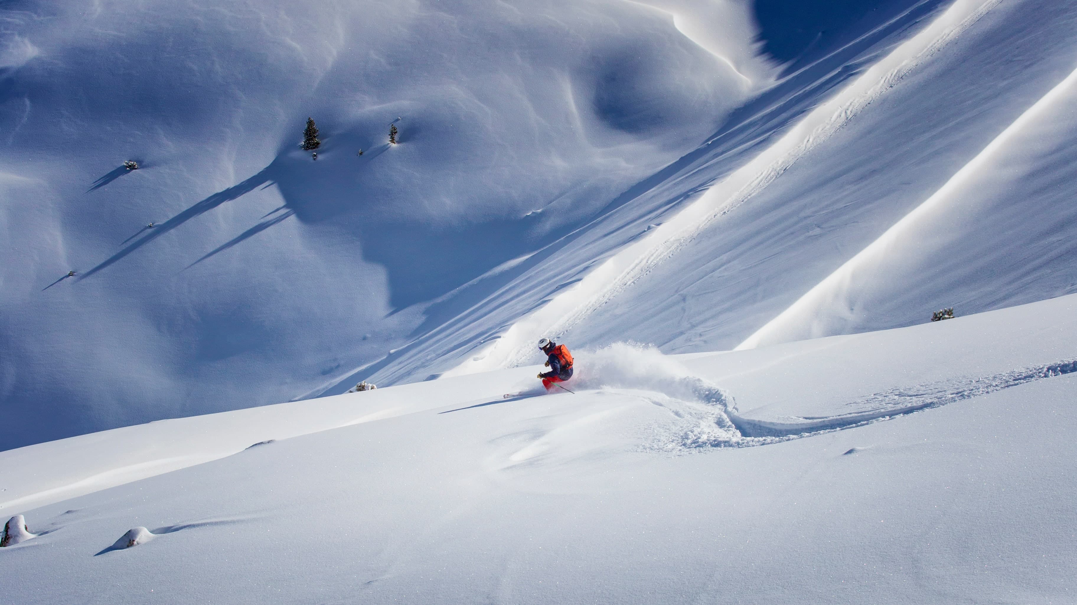 Far shot of a person skiing in the backcountry through untouched, thick powder